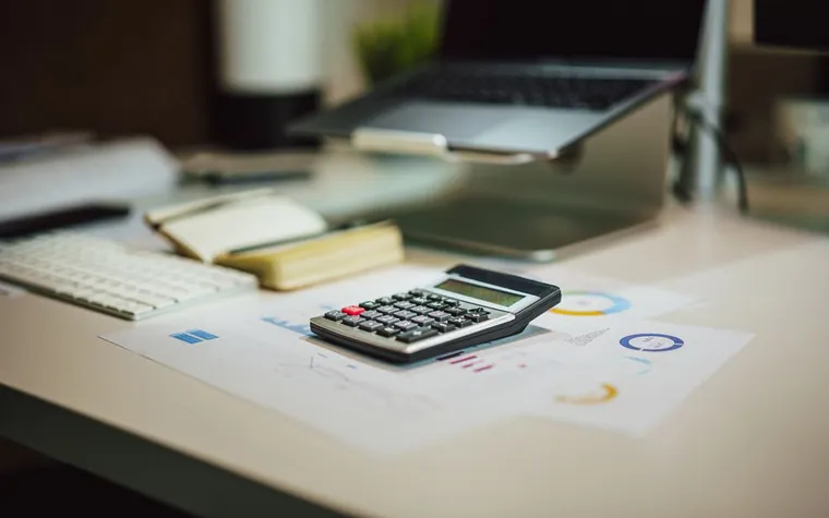 Mesa de trabalho com calculadora, notebook e documentos financeiros
