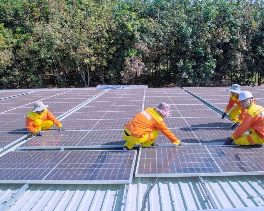 Equipe de instaladores fixando módulos fotovoltaicos na cobertura de um galpão